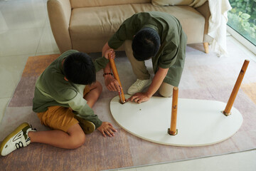 Son helping father to assemble small table for living room