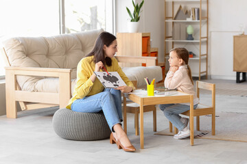 Female psychologist showing picture to little girl at table in office