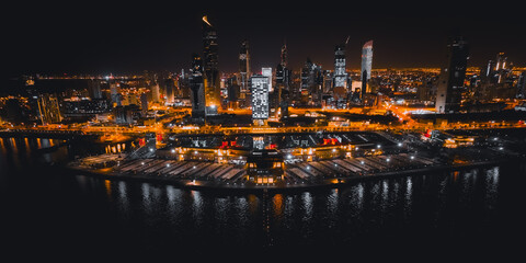 A colorful orange light aerial view of the Kuwait City skyline at night with a drone. - Powered by Adobe