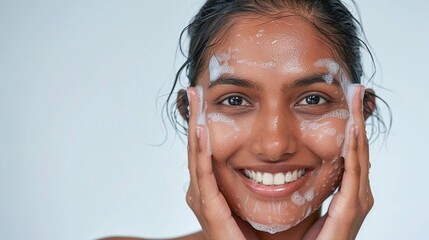 A smiling Sri Lankan woman with clear skin washing her face with soap on a grey background