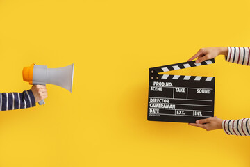 Hands with movie clapper and megaphone on yellow background