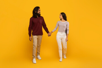 Couple walking hand in hand, yellow backdrop