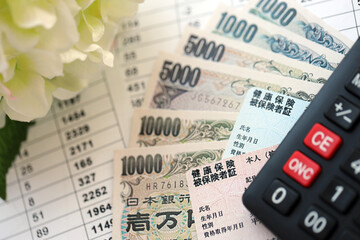 Light blue and red Japan Health Insurance cards on table with japanese yen money and calculator close up