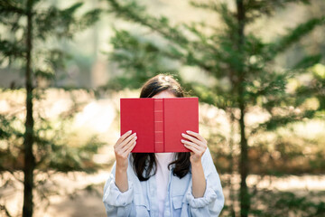 A person is holding a red hardcover book in front of their face