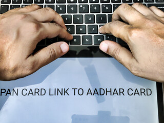 Picture of a person working on laptop. Placard with PAN CARD LINK TO AADHAR CARD written on it.