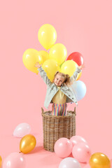 Happy little girl in basket with balloons on pink background