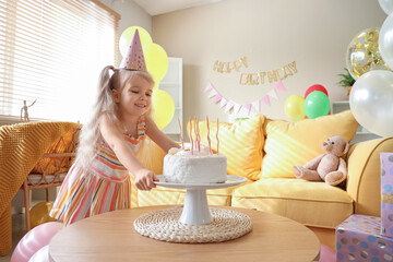 Cute little girl in party hat with cake, balloons and decorations for birthday at home