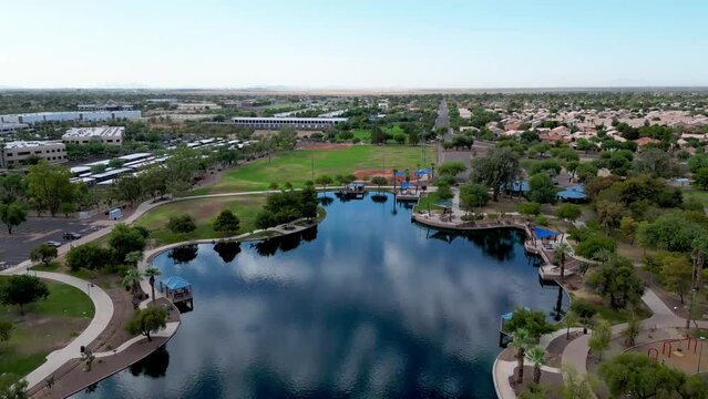 Drone of small lake surrounded by greenery with highway and buildings in Desert Breeze Park