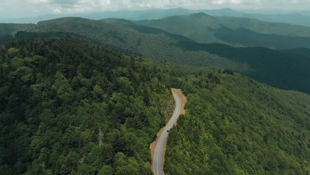 Drone following a car driving on a narrow road over green mountain in a beautiful terrain landscape