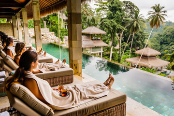 Relaxed women in bathrobes enjoying a serene spa retreat with a lush tropical backdrop and luxurious infinity pool. - obrazy, fototapety, plakaty