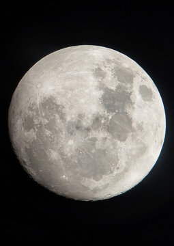 A high-resolution picture of the bright full moon shines in the dark sky, revealing its bumpy surface adorned with dark spots and bright spots reflecting light.