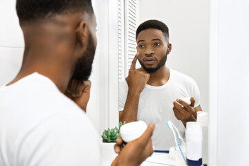 Man applying cream on face in mirror