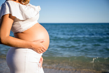 Pregnant woman with sun hat during her walk on the beach relaxing on her summer vacation, happy pregnancy outdoors.