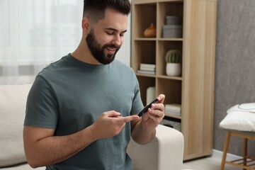 Diabetes test. Smiling man checking blood sugar level with lancet pen at home