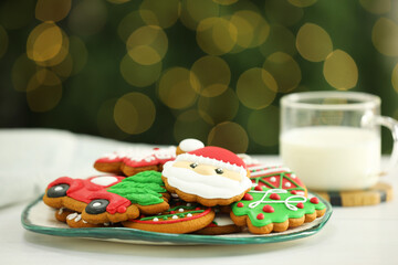 Decorated cookies and milk on white against blurred Christmas lights