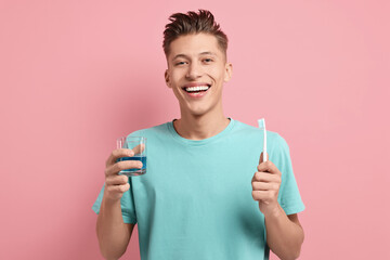 Young man with mouthwash and toothbrush on pink background