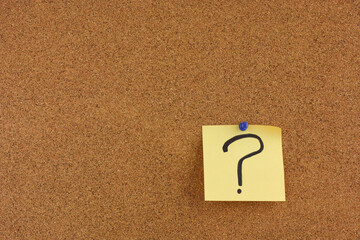 A yellow paper note with a question mark on it pinned to a cork board.