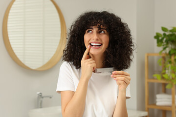 Young woman holding teeth whitening strips in bathroom
