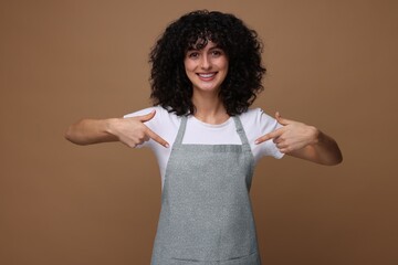 Happy woman pointing at kitchen apron on brown background. Mockup for design