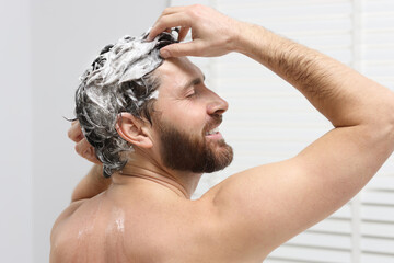 Happy man washing his hair with shampoo in shower