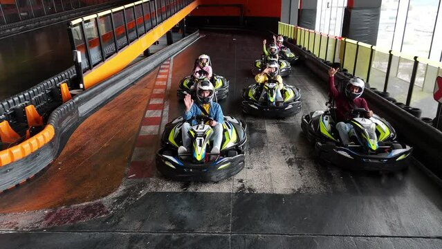 Drivers in helmets prepare for a go-kart race on an indoor track. Indoor Go-Kart Racing Competitors Lined Up at Starting Line