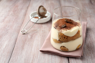Delicious tiramisu with coffee beans in glass on wooden table, space for text