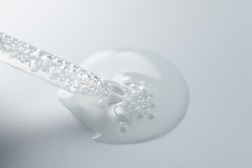 Dripping moisturizing serum from pipette on light grey background, closeup