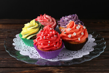 Delicious cupcake with bright cream on wooden table against black background