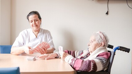Female caregiver playing cards with elderly woman in nursing home