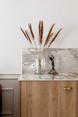 Twig plant in a hardwood vase on wooden cabinetry next to a statue
