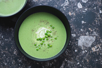 Black bowl with green pea cream-soup on a dark-brown granite background, horizontal shot with...