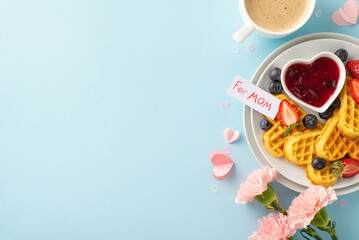 Mother's Day breakfast table: view from top showing heart-shaped waffles, fruit, jam, coffee, blooms, "for mom" greeting on a pastel blue setting, blank area for text