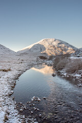 The River Coe in Glencoe reaching towards snow-covered mountains under a clear blue sky. Scottish Highlands, UK - obrazy, fototapety, plakaty