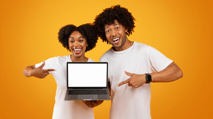 Positive millennial black couple holding laptop with blank screen