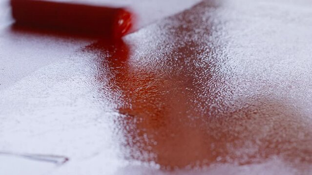 A construction roller applies paint to the surface. Construction work and painting of materials. Use red paint to paint a table or walls and floor.