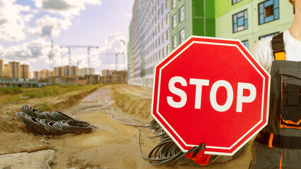 Stop sign in hand of builder. Construction site. Worker reports termination of construction. Travel...