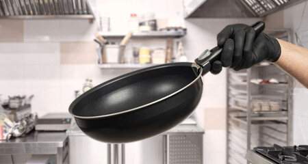 Frying pan in hand of cook. Professional kitchen utensils. Frying pan in restaurant kitchen....