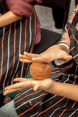 Children's hands knead a lump of clay for installation on a potter's wheel during a master class on an outdoor site