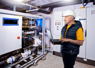 Man inspects boiler equipment. Engineer in factory basement. Engineering room with boiler...