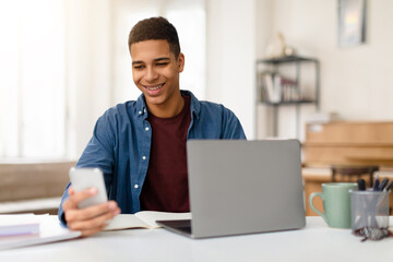 Man smiling at phone with laptop on desk