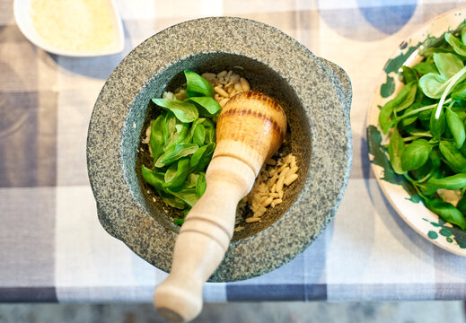 Preparation of traditional Pesto alle Genovese - with basil, olive oil, pine nuts, parmesan cheese and garlic crush in a mortar with a wooden pestle