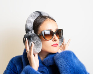 Winter fur earmuffs on woman in blue fur coat. Minimal fashion concept.