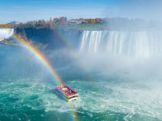 Niagara Falls. A pleasure boat with people near the huge famous waterfall. View from the Canadian side. A rainbow over the water on a sunny day. Nature scenery. Photo for advertising. - 772212333