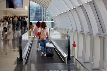 back view of travelers walking on escalator with suitcases and backpacks at singapore changi airport