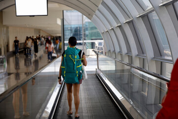 Young Asian traveler with backpack on airport escalator, big backpack and blank white tv screen....