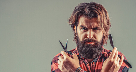 Man hairdresser in a plaid shirt holding a sharp professional scissors. Barber with straight razor...
