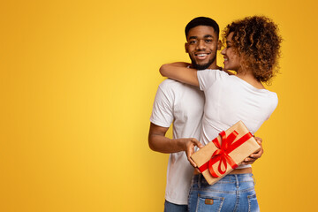 Black millennial couple with gift box on orange background - obrazy, fototapety, plakaty