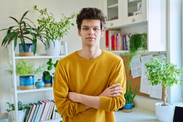 Portrait of young confident handsome guy with crossed arms, in home interior