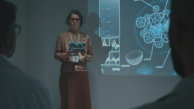 Medium full footage of Caucasian female pharmaceutical sales representative with tablet computer promoting new drug or therapy to doctors at medical conference, speaking about its benefits