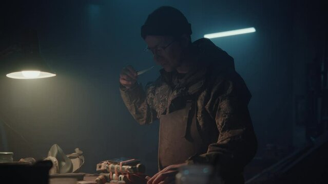 A man connects the phone to a bomb in his workshop at night